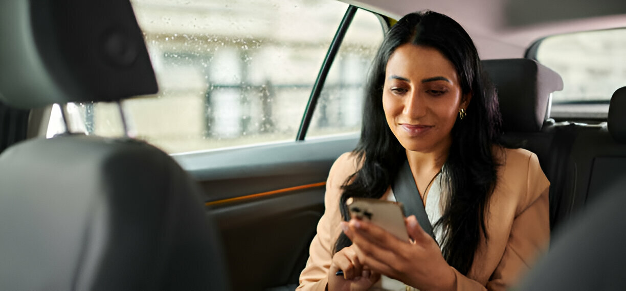A passenger in the back seat of a car, looking at a smartphone